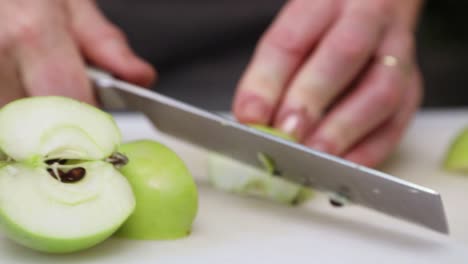 woman's hand with knife cutting green apple on chopping board in kitchen