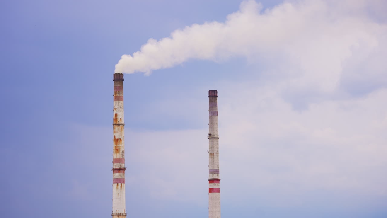 Old high pipes from industrial plant. Rusty pipes, one of which producing smoke into atmosphere. Blue sky backdrop.
