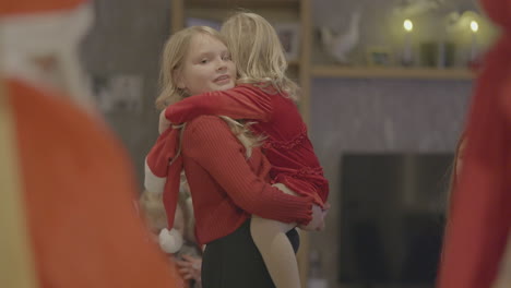 girl holds little sister as they wait for santa to give out christmas gifts