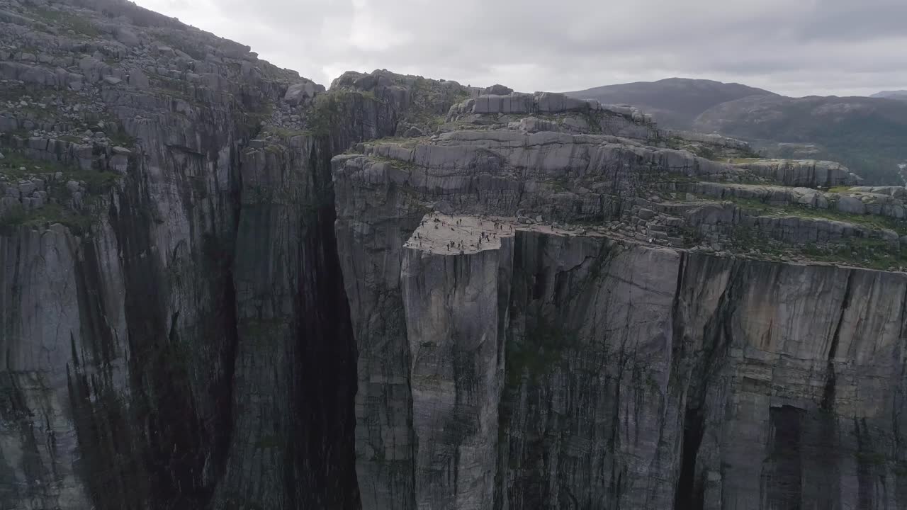 toma aérea en cámara lenta volando hacia preikestolen con turistas caminando y fotografiando el paisaje