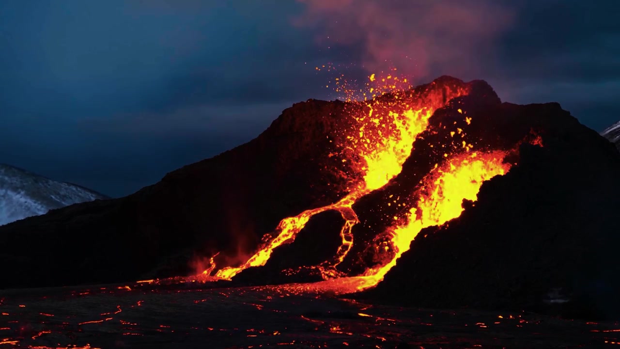 暗い火山の斜面を流れ落ちる溶岩と、夜空を埋め尽くす白熱した噴出物