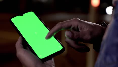 man scrolling on green screen mobile phone outdoors at night