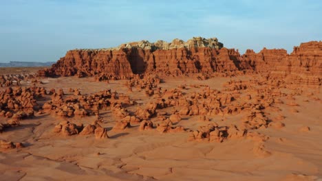 gorgeous trucking left aerial drone shot of the beautiful goblin valley utah state park with small strange mushroom rock formations below and large red and white butte's in the background