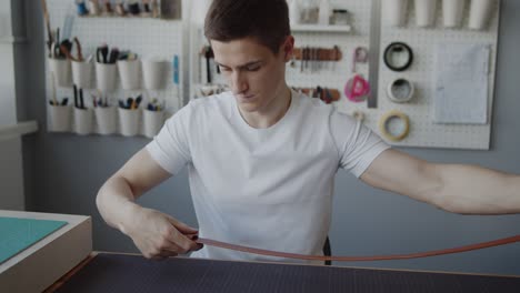 young leather worker putting a loop on a leather belt completing its making