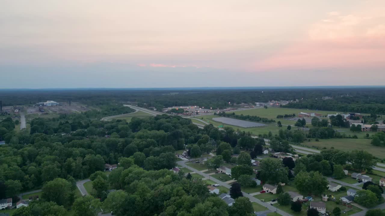 A scenic aerial view capturing a suburban area at sunset with sprawling green landscapes and distant city lights