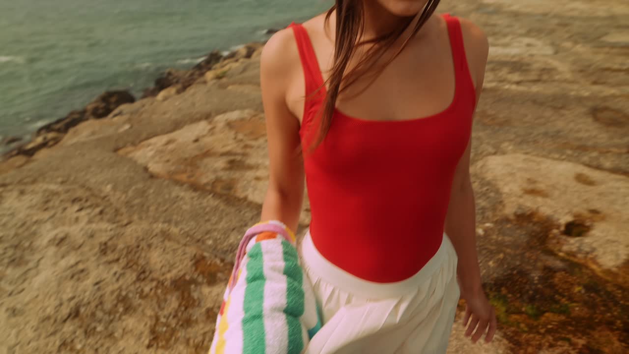 Mujer joven en traje de baño rojo caminando por un muelle rocoso junto al océano