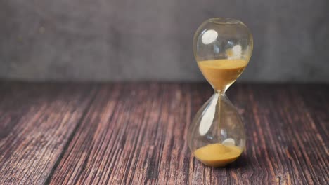 Hourglass-on-table,-sand-flowing-through-the-bulb-of-sandglass