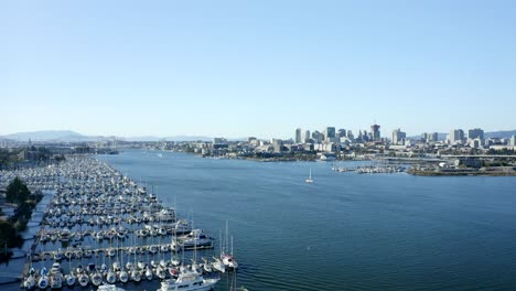 crane descending shot of the marina with sail boats in the foreground and the massive city in the backdrop