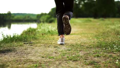 primer plano de pies corriendo en zapatillas a lo largo del río en el césped