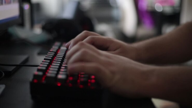 medium static shot of a young man using a mechanical keyboard with red leg lighting next to a led lighting mouse with blurred household elements
