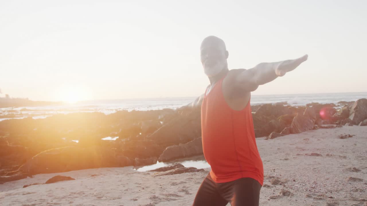 Uomo anziano afroamericano che fa yoga e stretching in spiaggia, al rallentatore