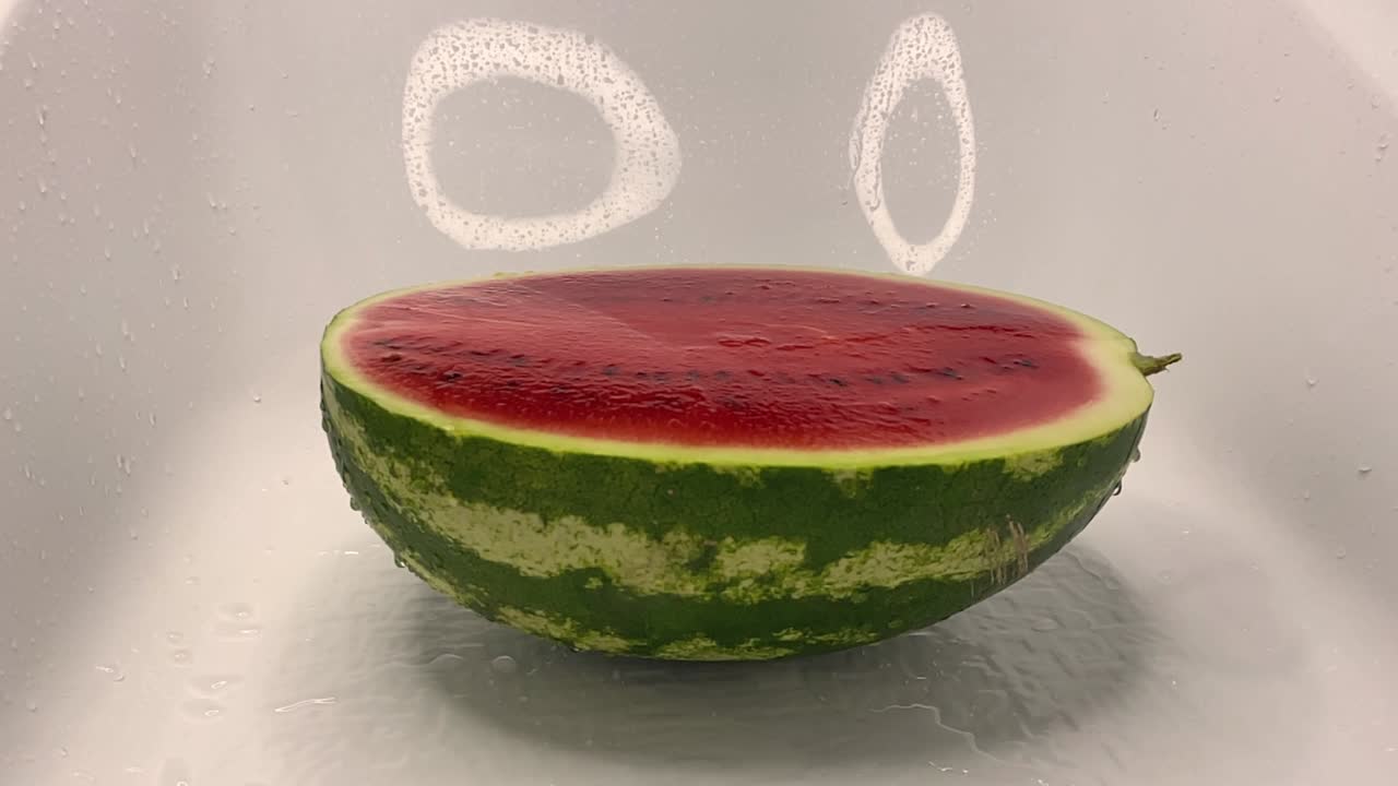 물의 제트가 잔한 은 익은 수박에 떨어지고 반으로 잘라서 스프레이를 떨어뜨립니다.