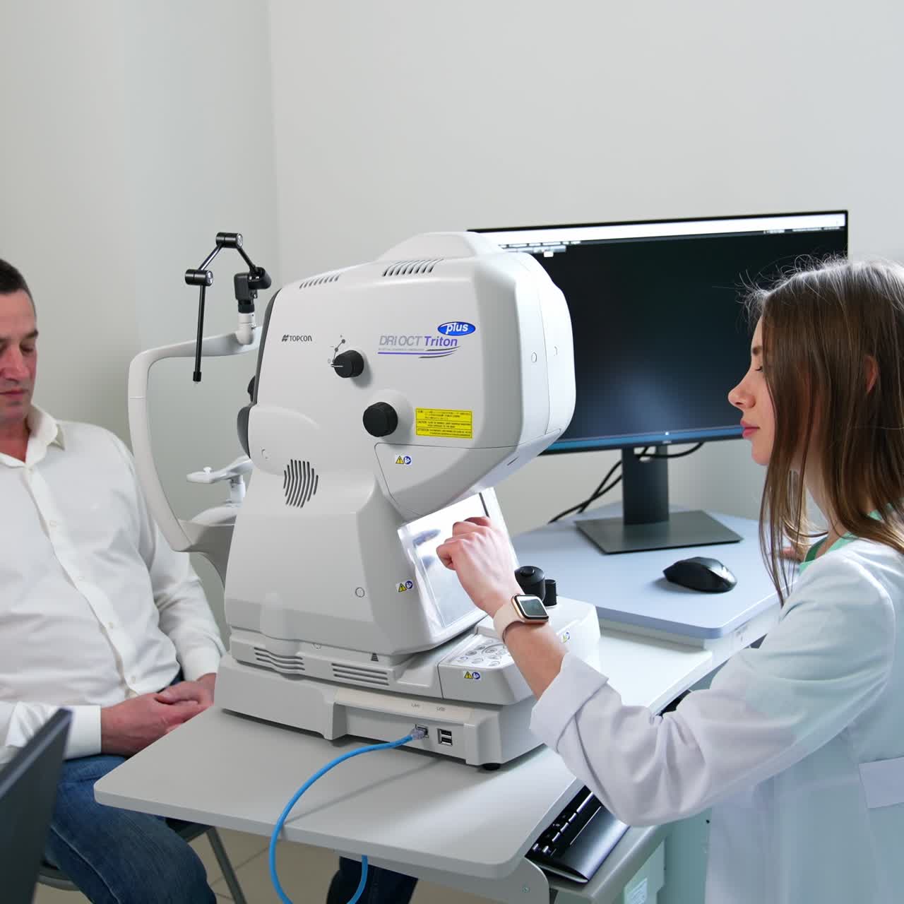 Young female ophthalmologist checks up man's eyesight. Patient moves closer to the apparatus at doctor's table