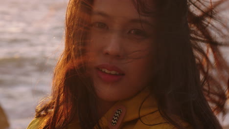 portrait of happy asian woman smiling enjoying vacation exploring travel lifestyle relaxing on beach feeling positive at sunset with wind blowing hair