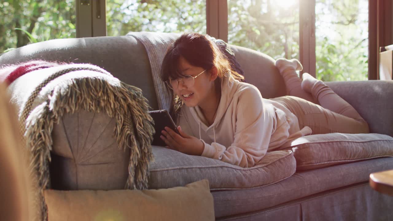 소파에 누워 태블릿을 사용하고 웃는 아시아 소녀