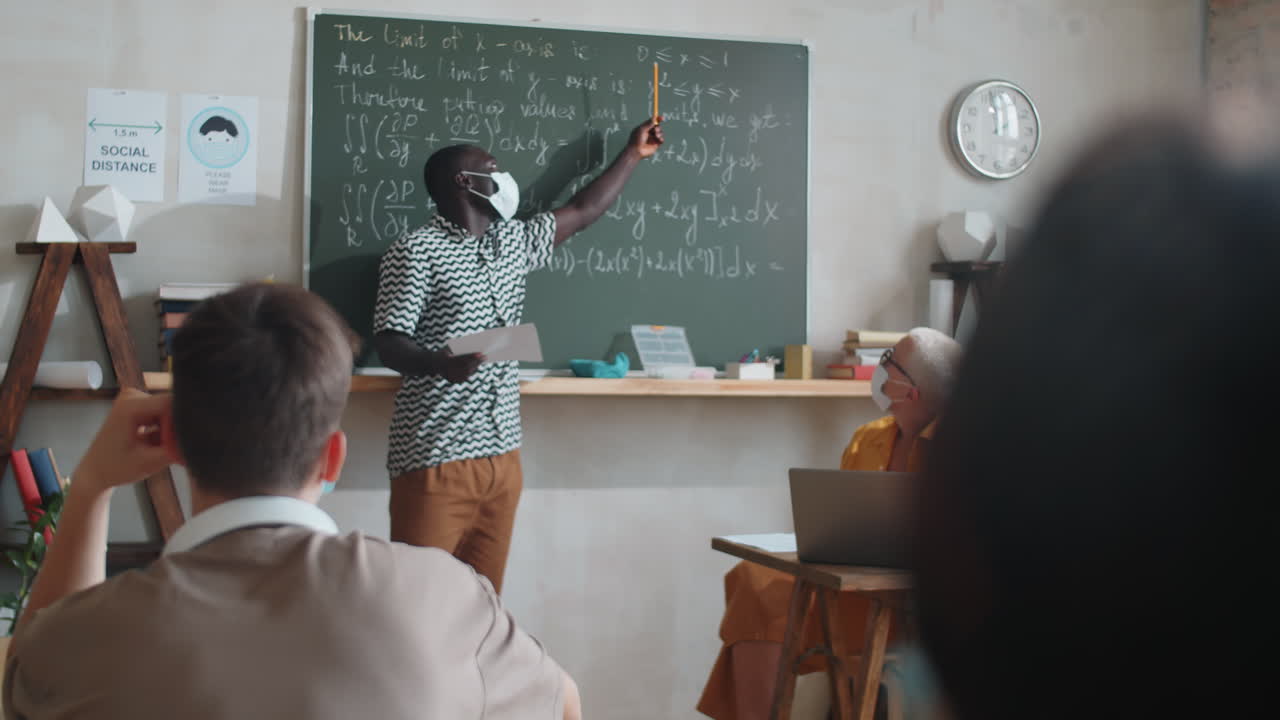 estudiante afroamericano con máscara tomando por la pizarra en la lección