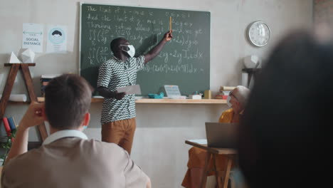 Afroamerikanischer-Student-In-Maske,-Der-Im-Unterricht-An-Der-Tafel-Steht