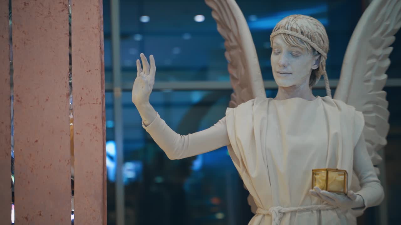 White angel living statue. Beautiful female live statue with wings near the tender flowers on the building background.
