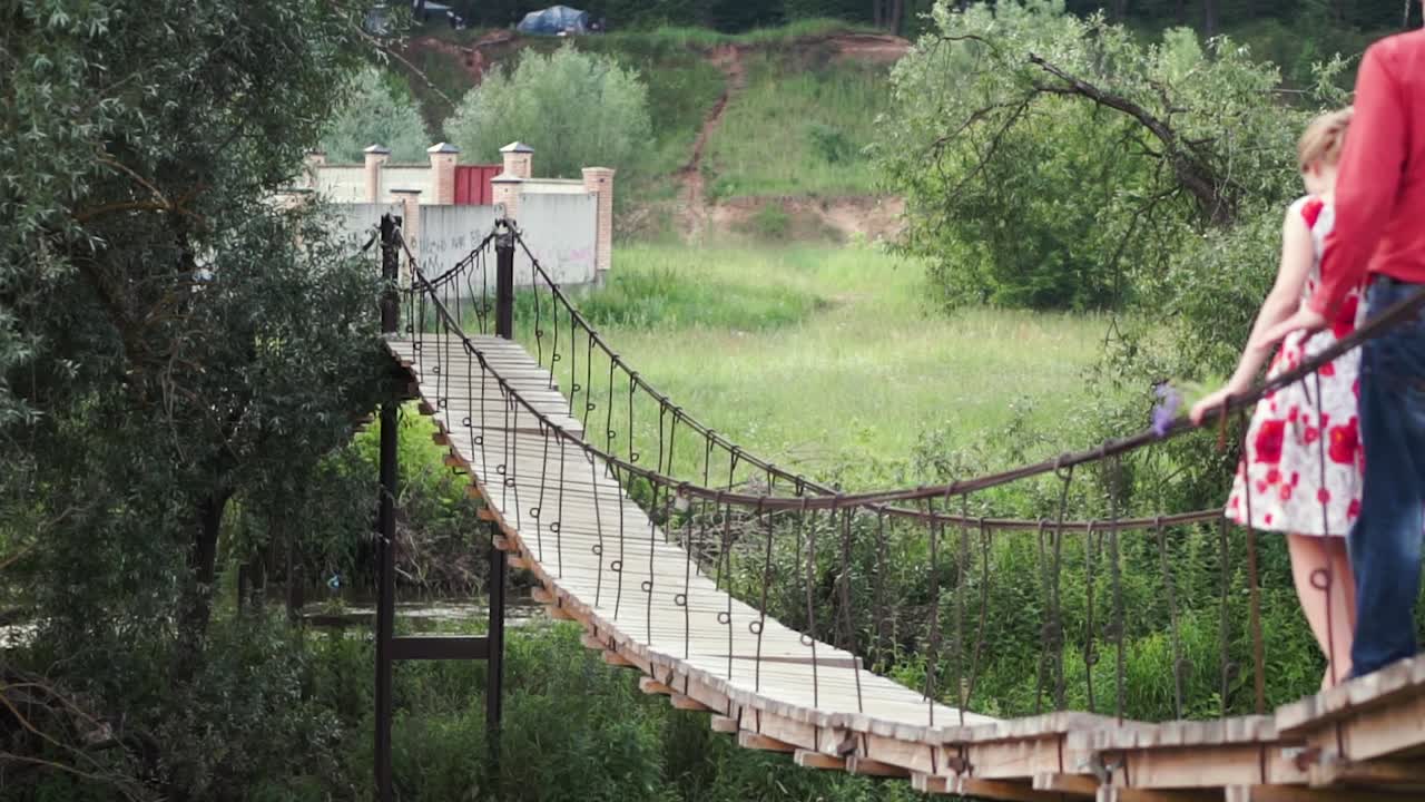 pareja caminando a través de un puente de cuerda de madera en la naturaleza