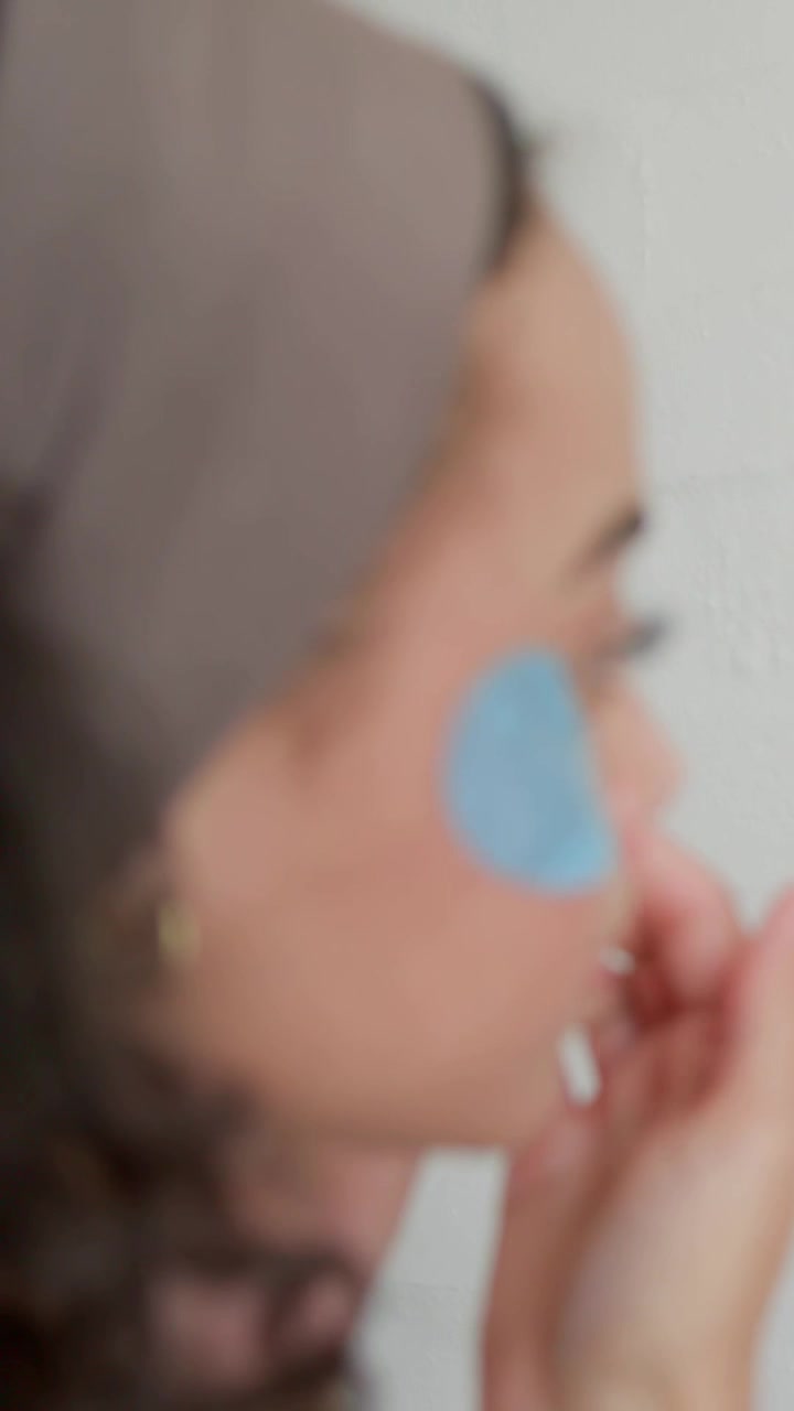 Vertical video: Applying band woman tucking blue left-eye patch for care at bath mirror, copy space