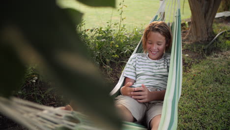 a boy relaxes in a hammock while looking at his phone