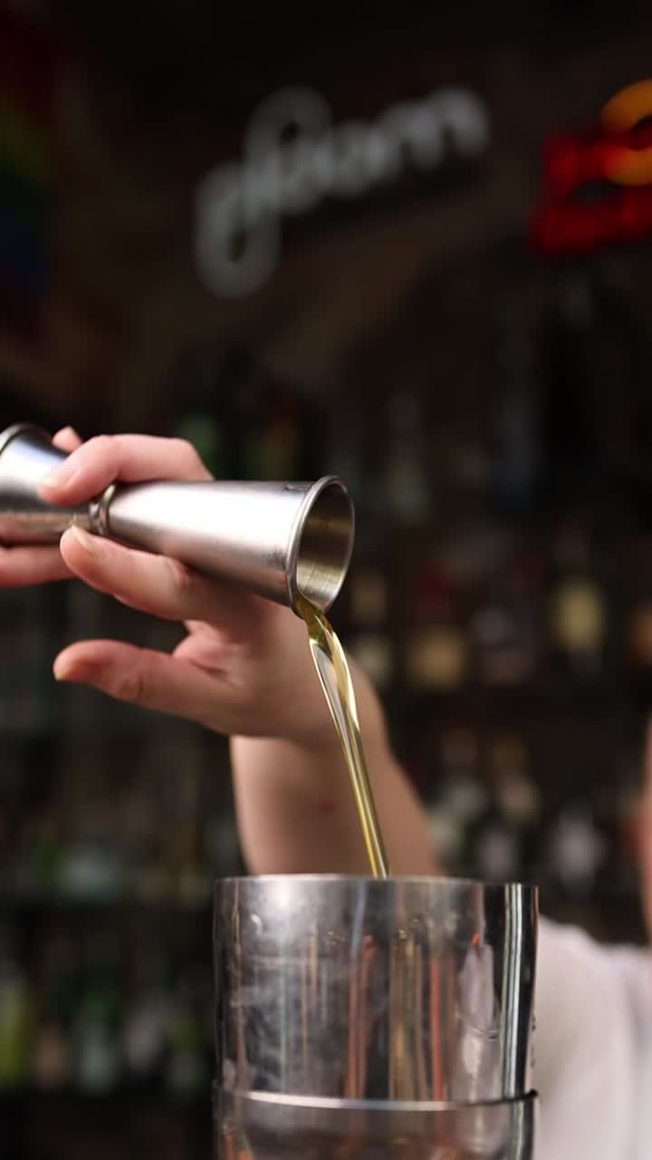 Barman che versa liquido da un jigger in uno shaker per cocktail.