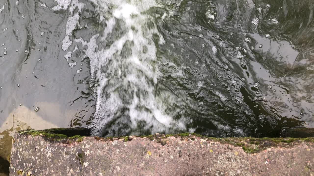 콘크리트 하수구를 통해 흐르는 물줄기, 공원의 오염된 물체, 위에서 가까이 찍은 사진.
