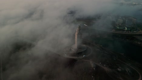 aerial view over clouds, misty view of historic lighthouse overlooking the city of coruña in spain, galicia