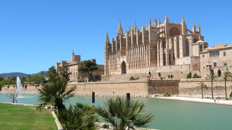 Santa-Maria-Le-Seu-cathedral-in-Palma,-palm-trees-and-fountain,-static