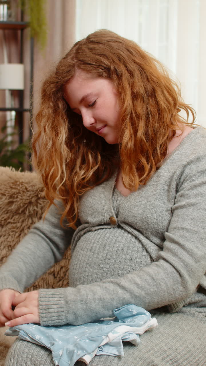 Pregnant woman sorting baby clothes at home smiling emotional expression preparing for motherhood