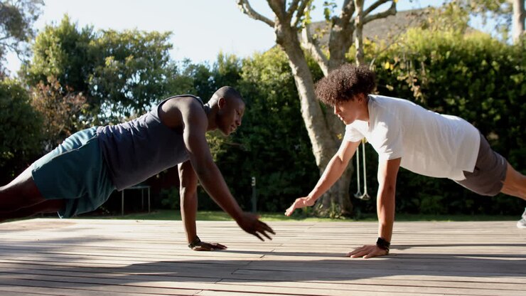 Exercising outdoors, two multiracial male friends doing push-ups together on wooden deck, copy space