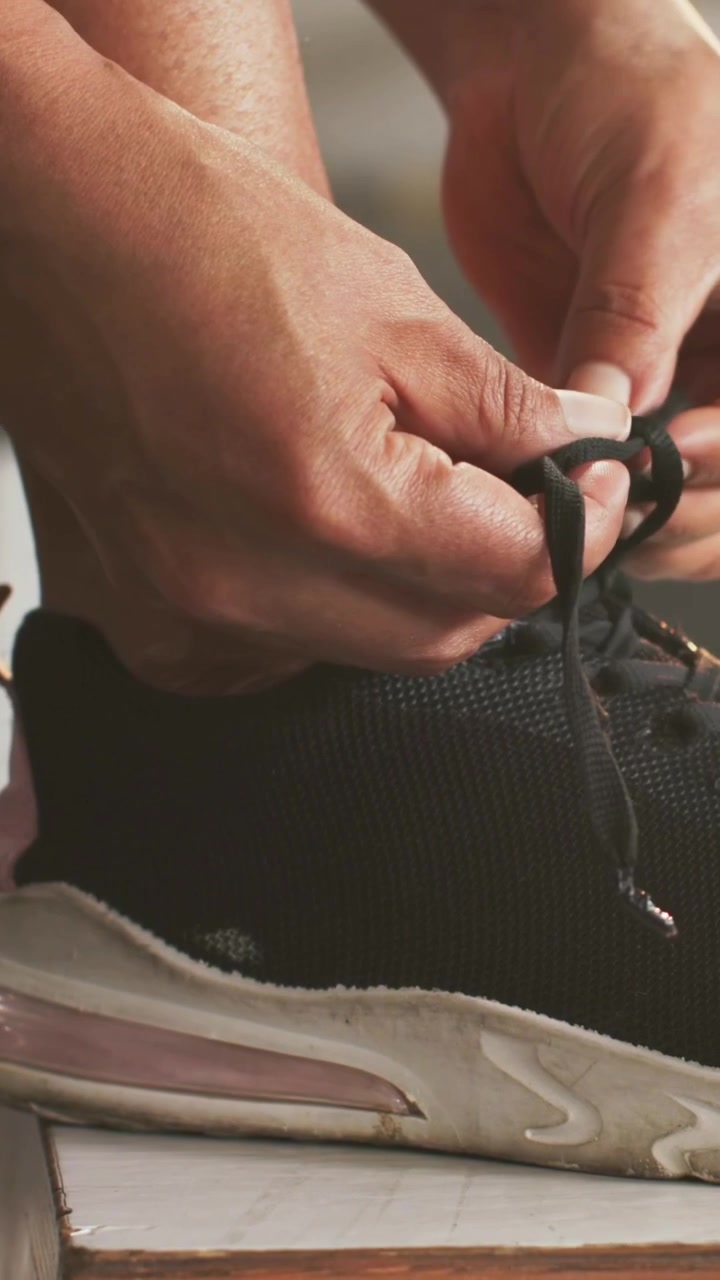 Video verticale: Tirando la scarpa da ginnastica di una donna, con il piede su una panca da palestra, infilando e allacciando i lacci per l'allenamento.