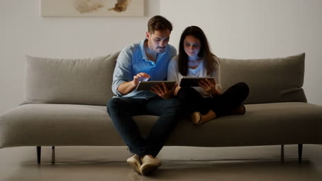 couple using tablets on a sofa at night