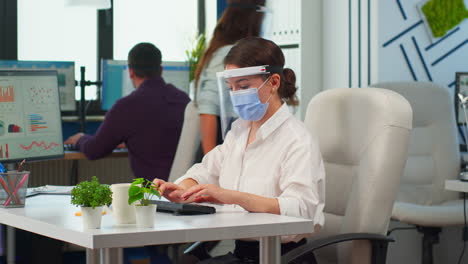gerente con máscara facial escribiendo en la computadora y mirando a la cámara