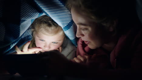 happy mother and daughter using tablet computer under blanket playing games on touchscreen technology relaxing having fun before bedtime