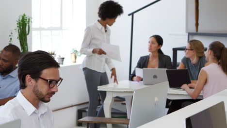 Woman-presenting-documents-to-colleagues-at-a-desk-in-office