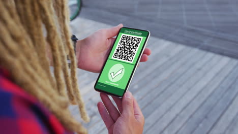 hombre con dreadlocks sosteniendo un teléfono inteligente con certificado de vacunación contra la covid y código qr en la pantalla