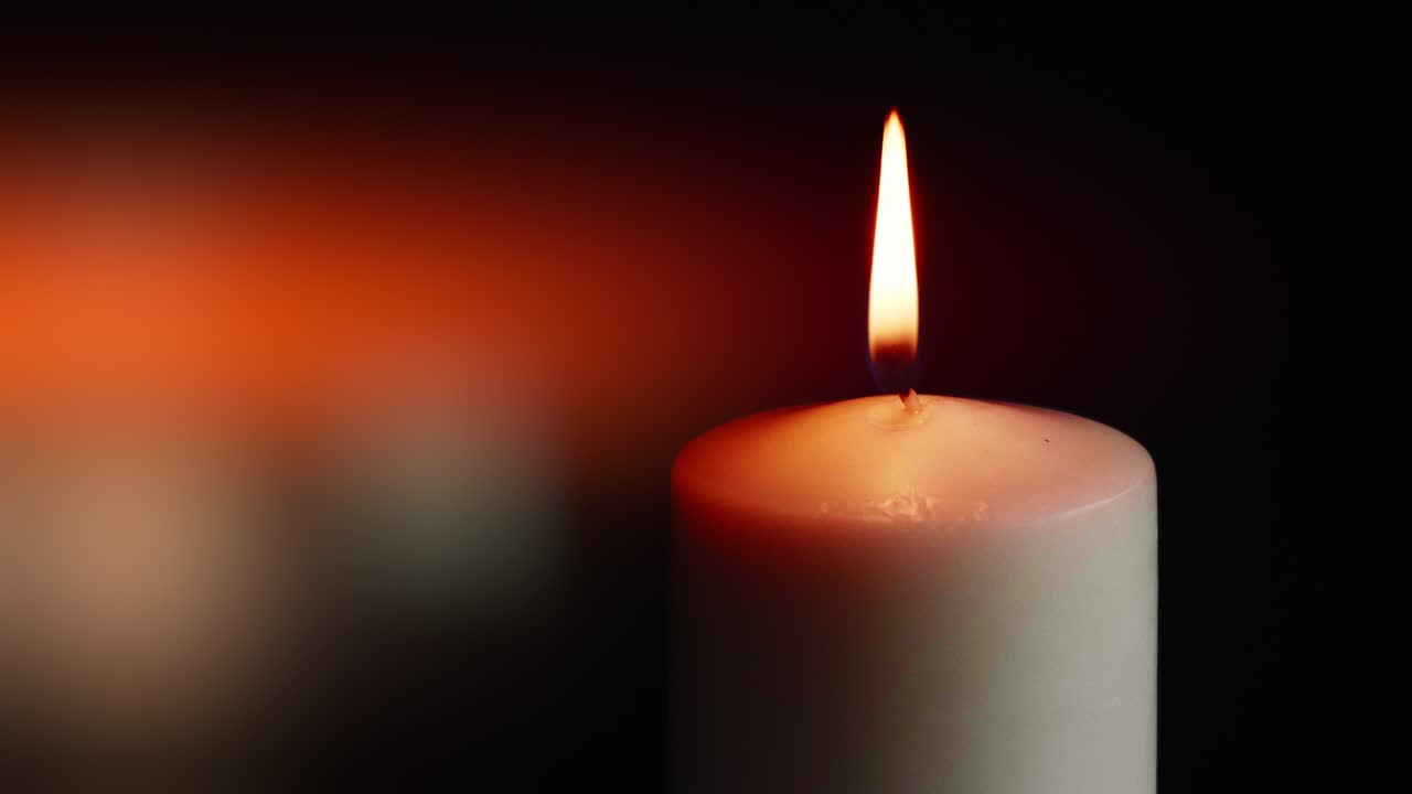 Přehlídka barevných jednotlivých svíček na černém pozadí s efektem světla a zpomaleného pohybu.