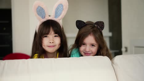 Caucasian-and-asian-looking-female-preschoolers-smiling-to-the-camera,-wearing-funny-bunny-ears