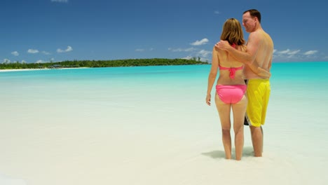 young caucasian couple walking on white sand beach