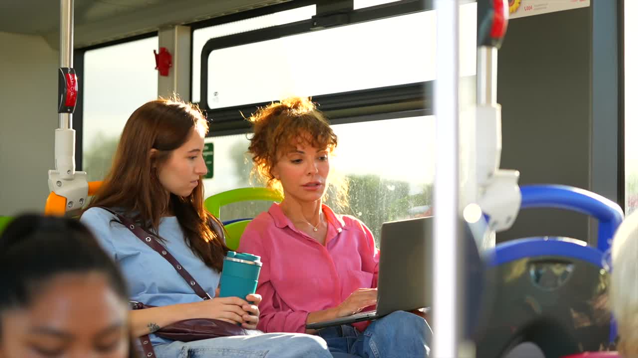 Two Women Chatting on a Bus While One Uses a Laptop