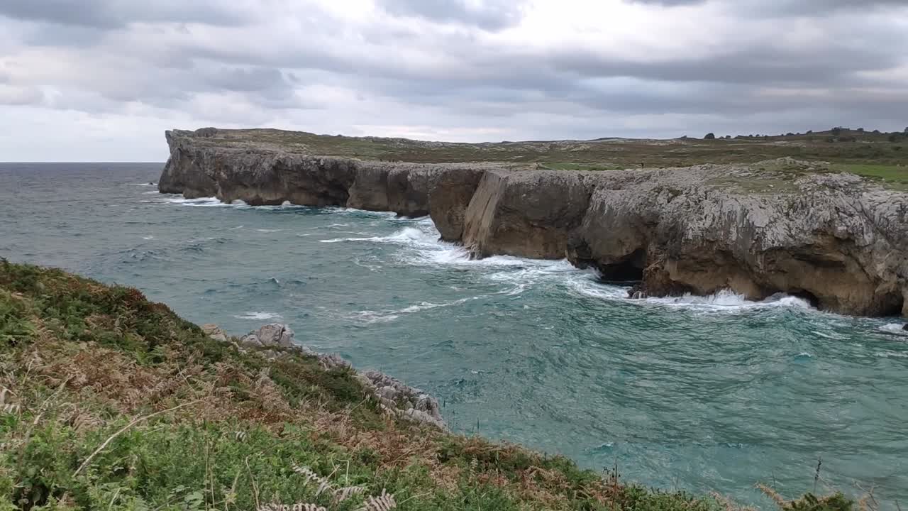 Rocky ocean cliffs, waves crashing at Guadamia cliffs in Asturias under cloudy sky