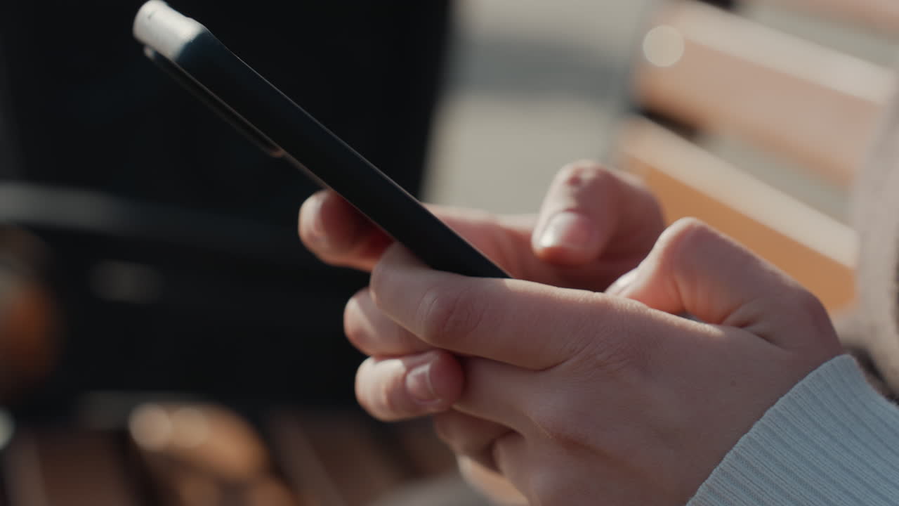 Mani che scorrono il telefono. Primo piano di mani che navigano sullo schermo dello smartphone. Un pendolare urbano si ferma per scorrere il dispositivo mobile. Scatto dettagliato di mani che scorrono lo smartphone mentre sono sedute su una panchina in città.