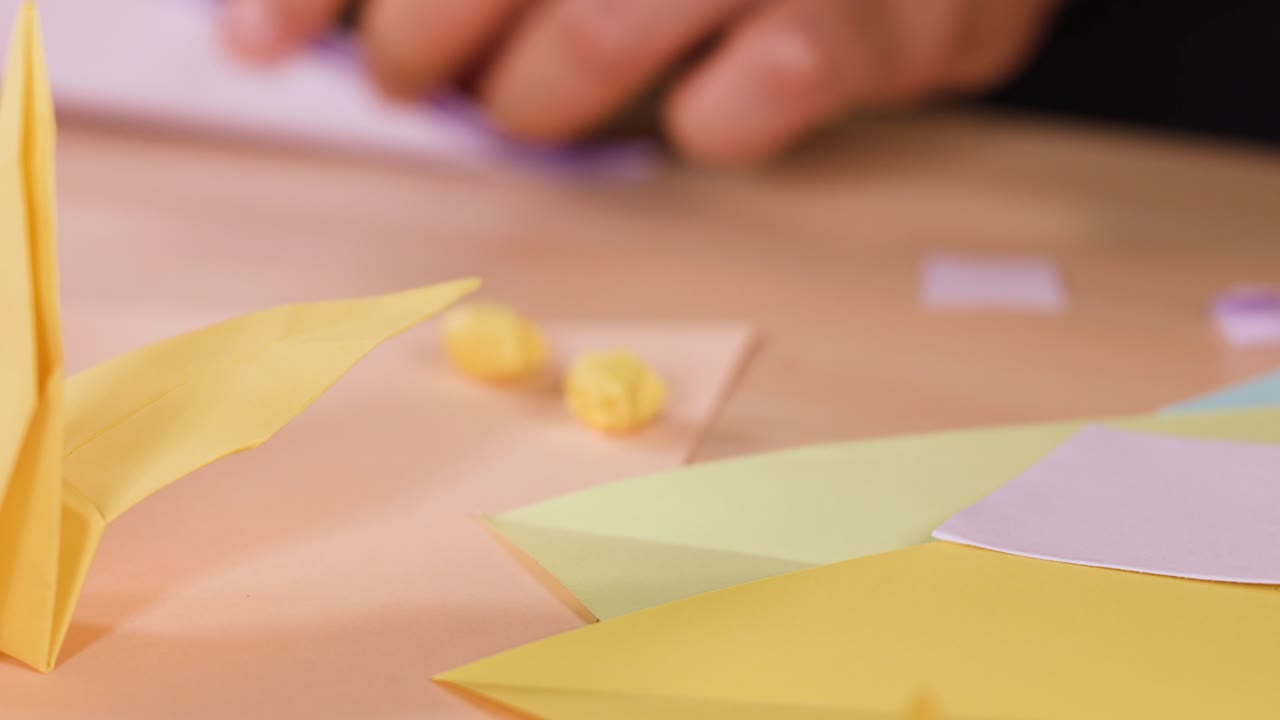 Primo piano di mani che piegano carta su un tavolo di legno dietro una gru origami gialla