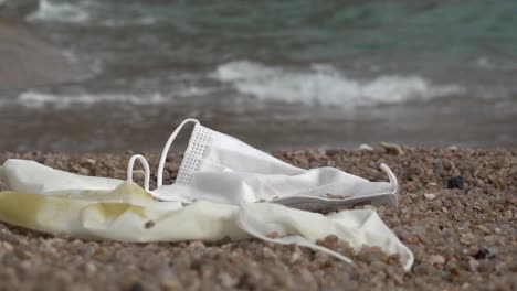 discarded mask and glove on a beach with continuous rushing wave nearby, steady shot moving right