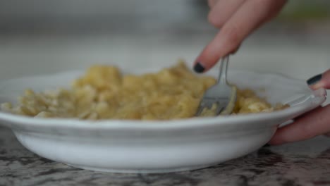 Close-up-side-view-of-hand-mushing-banana-with-fork-in-porcelain-bowl