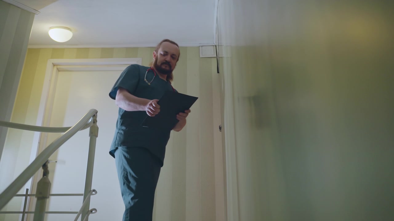 Infermiera afroamericana scende le scale di casa documentando, con un tablet in mano, si ferma alla porta per controllare gli appunti, effettua una telefonata alla centrale operativa, con maniera professionale e delicata, illuminazione calda del corridoio e atmosfera tranquilla di assistenza domiciliare