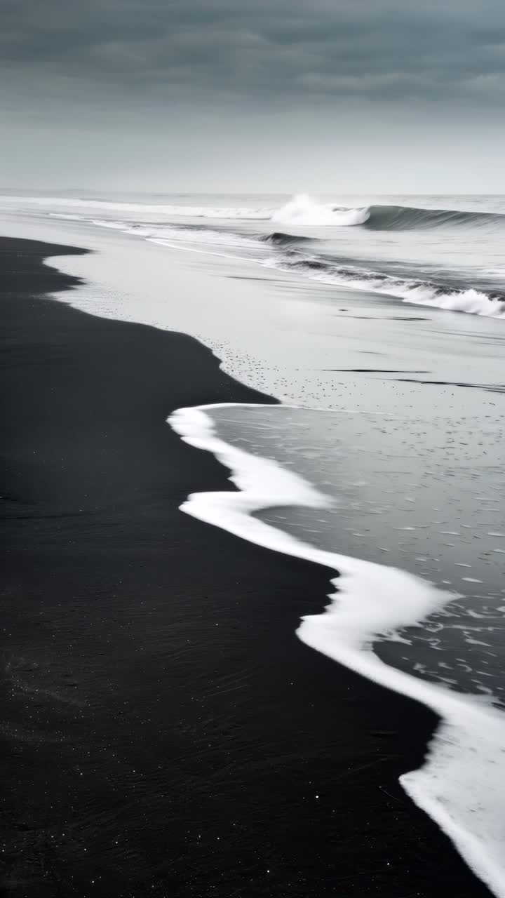 A serene video still of a black sand beach with gentle waves, captured from a low angle
