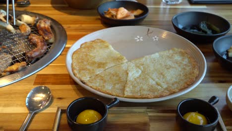 grilling korean chicken barbecue with egg yolk, side dish, and korean potato pancake on table in restaurant in chuncheon city, south korea