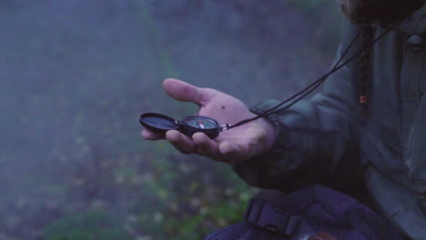 Long-bearded-man-looking-at-the-compass-in-woodlands-forest-with-fogs,-dolly-out